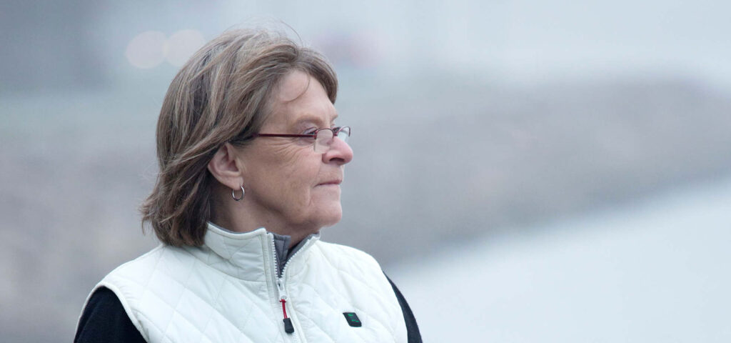Asmuo dėvi baltą dygsniuotą liemenę iš NordicHeat. Dėmesys komfortui ir šilumai lauko aplinkoje. Aktyvus gyvenimo būdas pabrėžiamas per funkcionalius žiemos drabužius. Nėra matomo teksto.