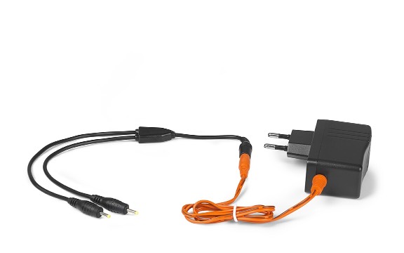 Juodas ir oranžinis įkrovimo adapteris su dviguba kabelio išvestimi, tikriausiai prijungtas arba tinkamas NordicHeat šiltiems drabužiams neutralioje aplinkoje.