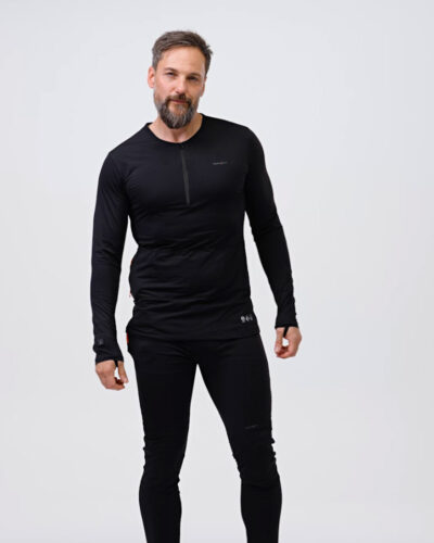 A man wearing black NordicHeat thermal clothing stands upright in a neutral, bright studio environment. The outfit consists of a long-sleeved shirt and pants designed for warmth.