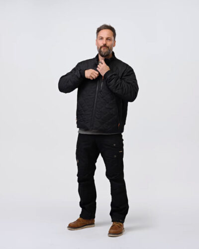 A person wearing a black quilted jacket and pants stands against a white background, adjusting the jacket at the neck. The person has brown hair and a beard.
