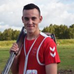 A person in a red Hummel t-shirt and target vest carries a rifle outdoors. Suitable for active lifestyles, NordicHeat can provide warm clothing for similarly chilly outdoor activities. Text: Team Denmark.