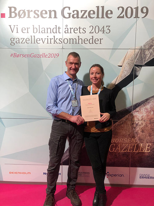 Two people stand in front of a background with the text "Børsen Gazelle 2019". They hold a diploma indicating that they are among this year's 2043 gazelle companies.