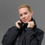 A person wearing a black NordicHeat jacket adjusts the collar. The background is neutral gray, highlighting the jacket as the main motif.