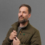 A person wearing a green NordicHeat jacket zips up in a neutral gray background.