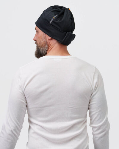 Person wears a black NordicHeat beanie that promotes warmth and comfort for active lifestyles. Text: "NORDICHEAT". Casual context focusing on practical clothing in a cool environment.