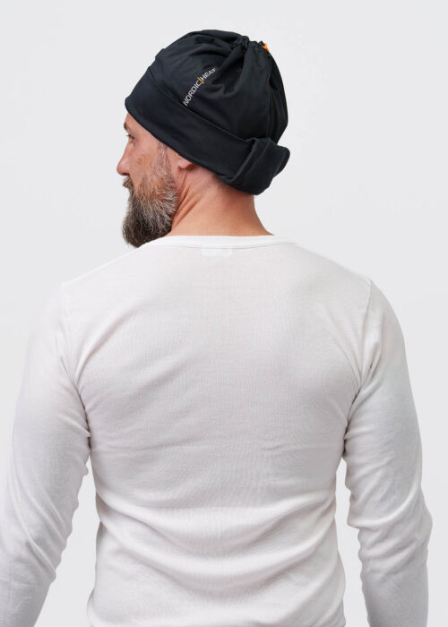 Person wears a black NordicHeat beanie that promotes warmth and comfort for active lifestyles. Text: "NORDICHEAT". Casual context focusing on practical clothing in a cool environment.