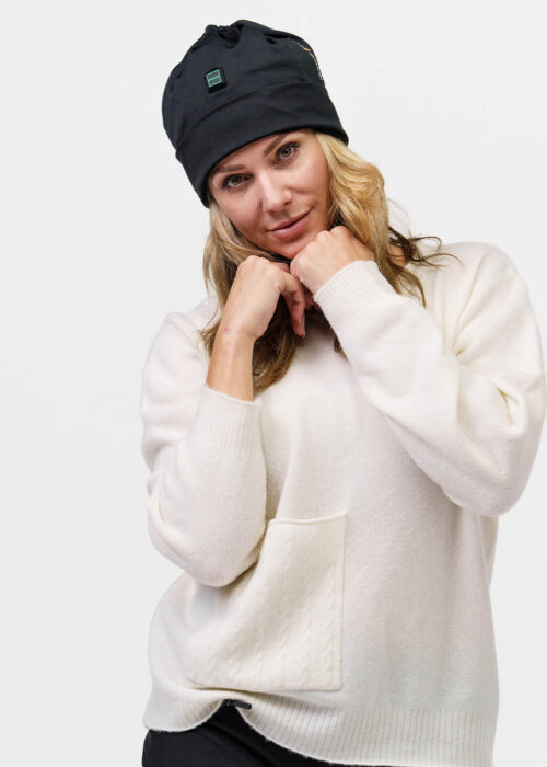 Person wears black NordicHeat warming beanie suitable for an active lifestyle. The cap has a green logo on the front. The person is dressed in a light sweater.