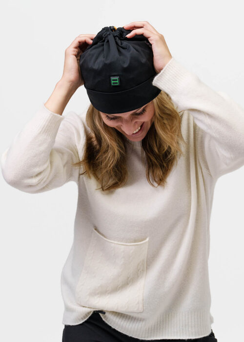 Person adjusts black NordicHeat beanie with heating panel, dressed in white sweater, symbolizing active lifestyle and practical winter clothing.
