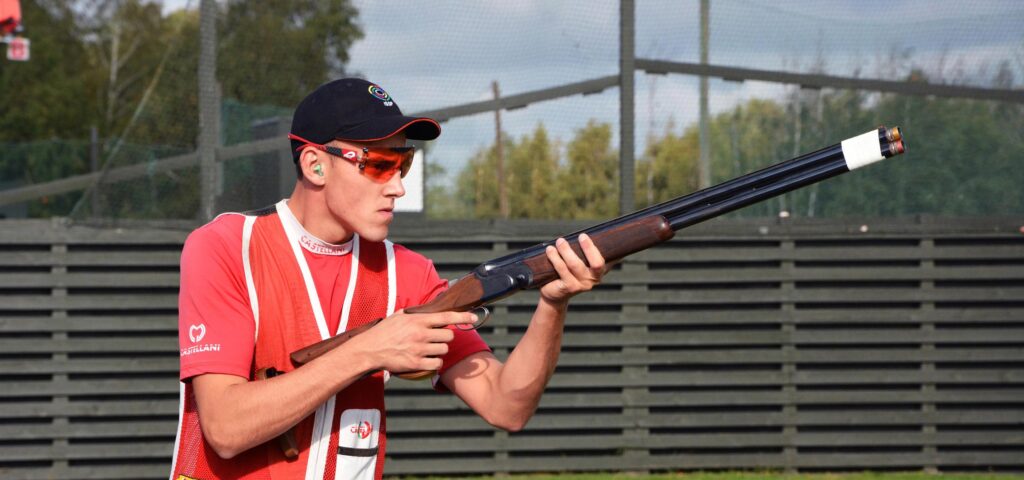 Asmuo, dėvintis NordicHeat termo drabužius, taikosi su sportiniu šauliu lauko šaudymo varžybose. Šiluma padeda išlaikyti dėmesį ir rezultatus. Matomas tekstas: "CASTELLANI".